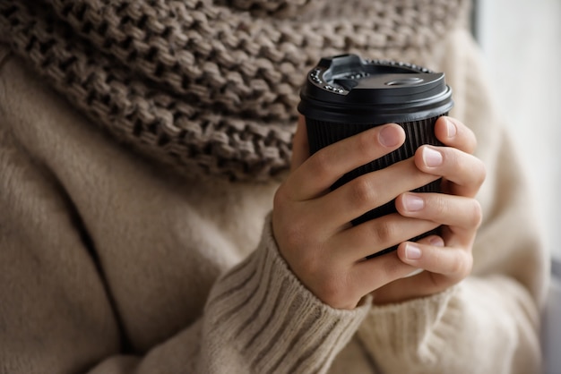 La muchacha sostiene una taza de papel con café.