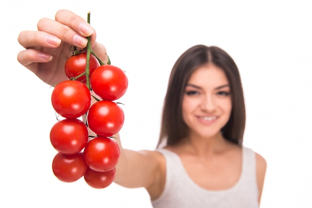 La muchacha sostiene los tomates en manos y sonríe.