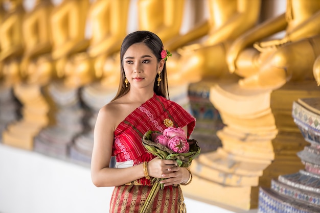 Muchacha tailandesa en la mano tailandesa tradicional del traje que sostiene loto en el templo tailandés, cultura de identidad de Tailandia.