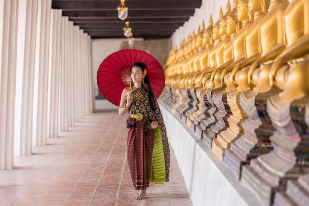 Muchacha tailandesa en traje tailandés tradicional con el paraguas rojo en el templo tailandés, cultura de identidad de Tailandia.