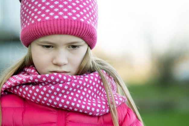 Muchacha triste del niño en ropa de invierno de punto caliente al aire libre.