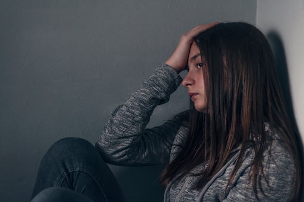 Foto muchacha triste sentada en el piso en la esquina de la habitación