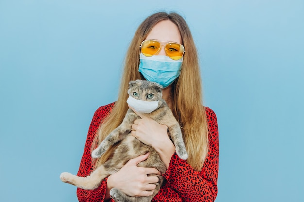 La muchacha en un vestido rojo con una máscara médica en su cara sostiene un gato.
