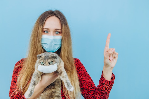 La muchacha en un vestido rojo con una máscara médica en su cara sostiene un gato.