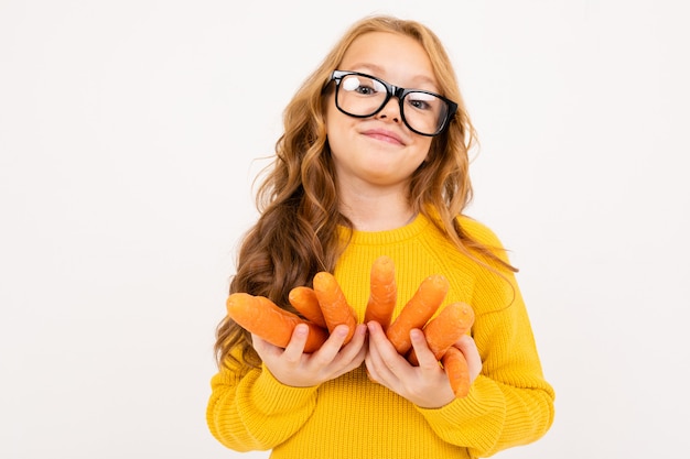 La muchacha en vidrios sostiene las frutas de la zanahoria en un fondo blanco aislado