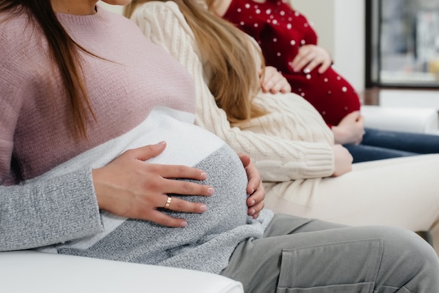 Las muchachas embarazadas sostienen sus barrigas con sus manos en primer plano. Clase prenatal de chicas embarazadas.