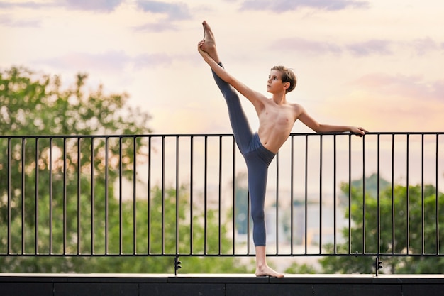 Foto muchacho adolescente del bailarín de ballet que ejercita en el fondo del cielo del atardecer en la azotea