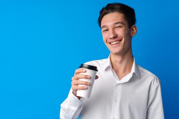 Muchacho adolescente bebiendo una taza de café sobre fondo azul.