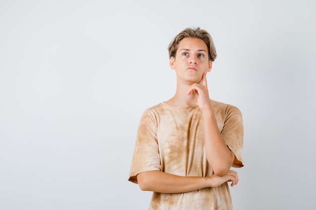 Muchacho adolescente en camiseta de pie en pose de pensamiento y mirando pensativo, vista frontal.