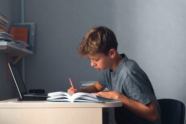 Muchacho del adolescente del estudiante que hace los deberes con el cuaderno abierto de la computadora portátil y el lugar de trabajo de la computadora en casa