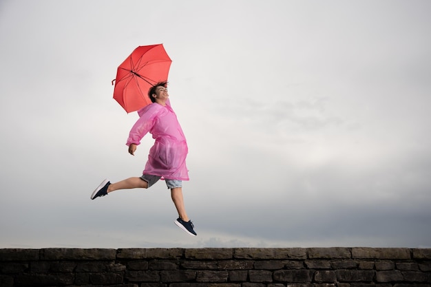 Muchacho adolescente feliz saltando y sosteniendo paraguas