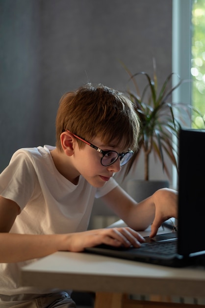 Muchacho adolescente con gafas juega con entusiasmo juegos de computadora. El colegial hace la tarea en la computadora. Educación en el hogar.