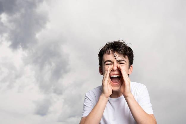 Muchacho adolescente gritando bajo el cielo dramático