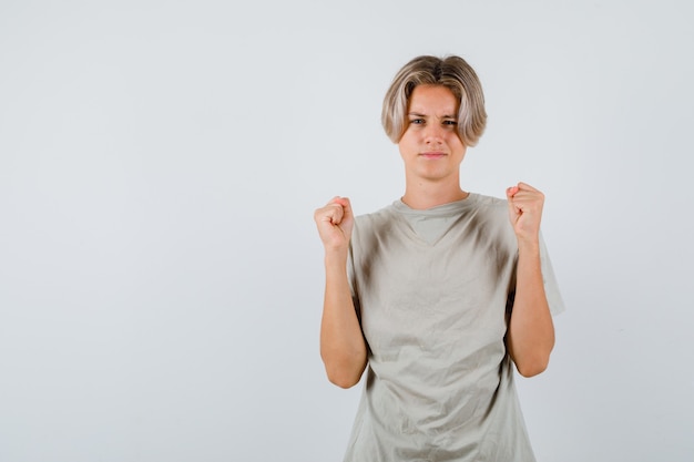 Muchacho adolescente joven que muestra el gesto del ganador en la camiseta y que parece afortunado, vista frontal.