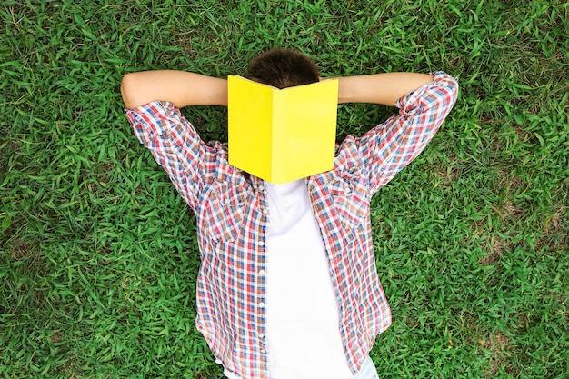 Foto muchacho adolescente con libro tumbado sobre la hierba verde