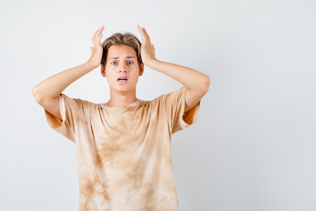 Muchacho adolescente lindo que mantiene las manos en la cabeza en la camiseta y que parece preocupado. vista frontal.