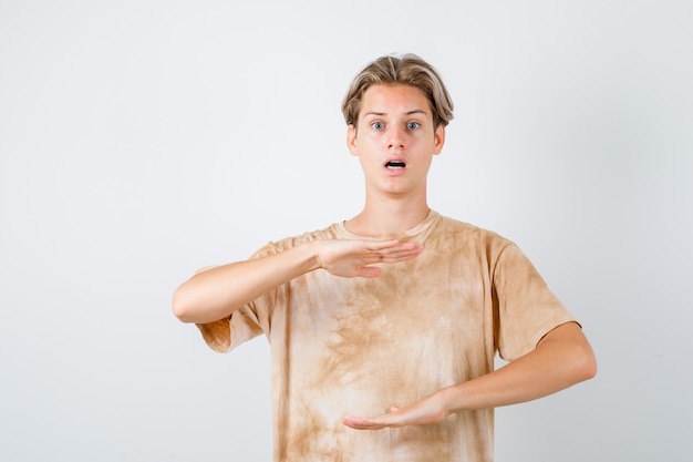 Muchacho adolescente mostrando signo de tamaño en camiseta y mirando perplejo, vista frontal.