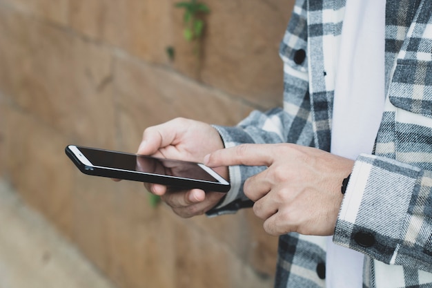 Muchacho adolescente que usa el dispositivo del teléfono inteligente para la tecnología de red en línea internet; el hombre usa el móvil en el parque público.