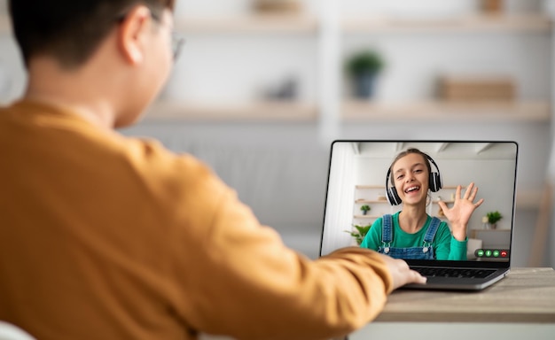 Muchacho adolescente sentado en el escritorio con videoconferencia portátil con una niña linda