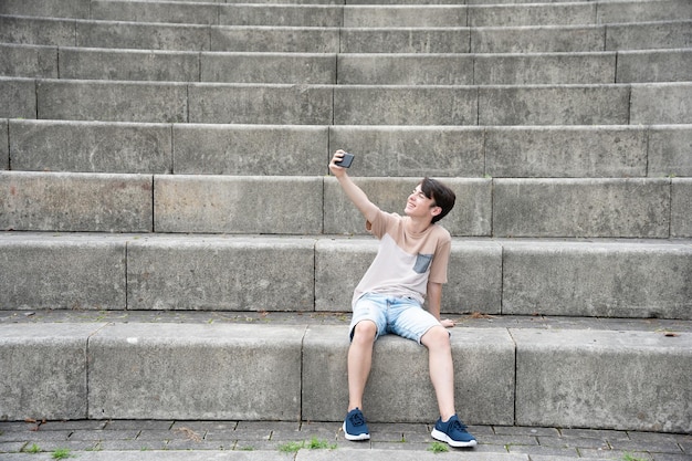 Muchacho adolescente tomando selfie sentado en la tribuna