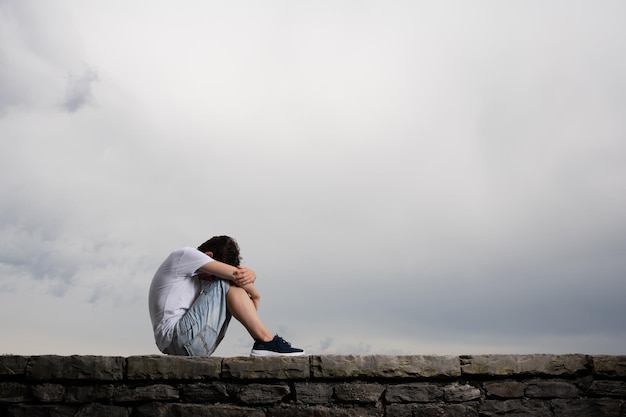 Muchacho adolescente triste que se sienta bajo el cielo dramático