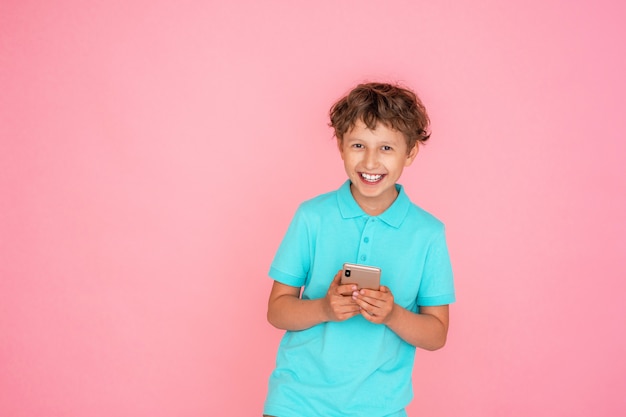 Muchacho alegre con el pelo ondulado, sosteniendo un teléfono inteligente en un rosa.