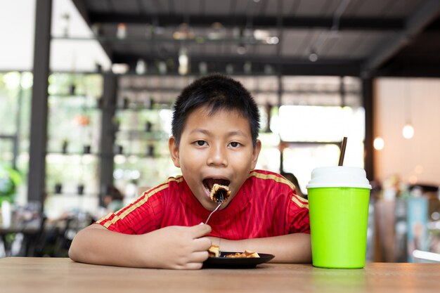 El muchacho asiático de la cara feliz goza el comer de la galleta del chocolate en restaurante.