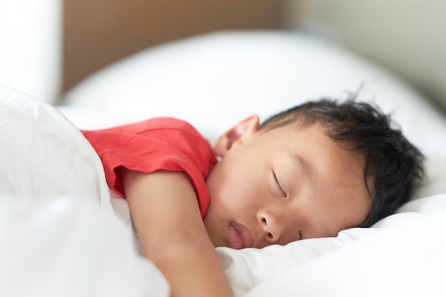 El muchacho asiático duerme o toma una siesta en una almohada cómoda y una cama en sueño profundo