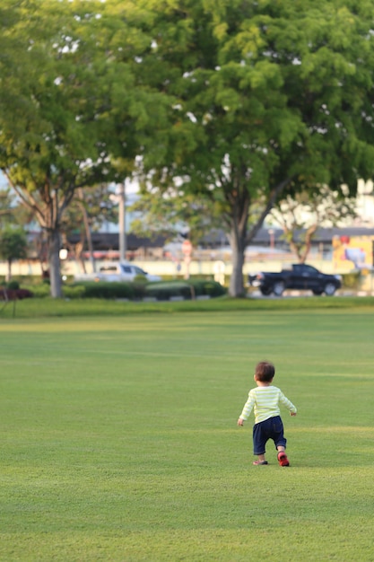 El muchacho asiático está aprendiendo a caminar en el jardín.