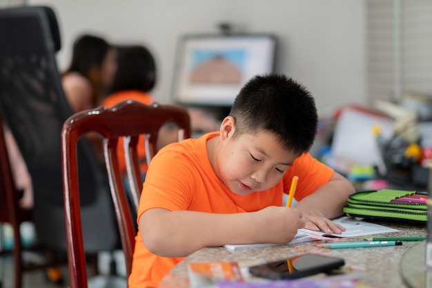 Muchacho asiático haciendo la tarea, papel de escribir infantil, concepto de educación, regreso a la escuela