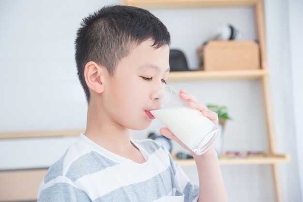 Muchacho asiático joven que bebe un vidrio de leche para el desayuno