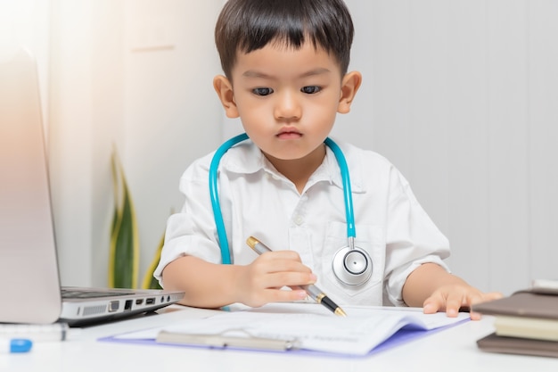 Foto muchacho asiático joven que juega al doctor y que escribe en carta de diagnóstico.