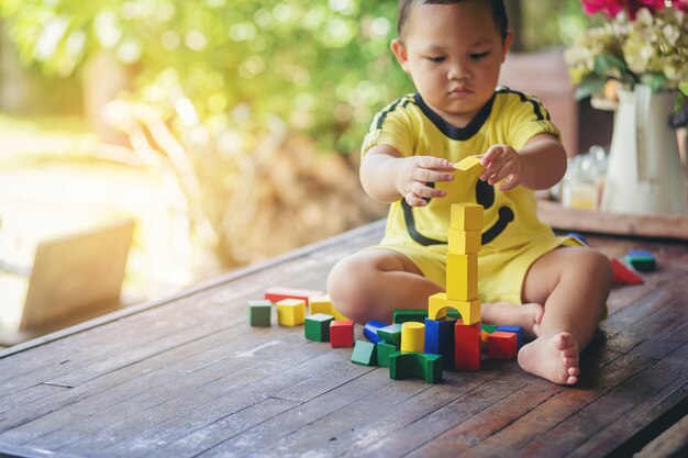 El muchacho asiático lindo intenta jugar con el bloque de madera colorido. Educación