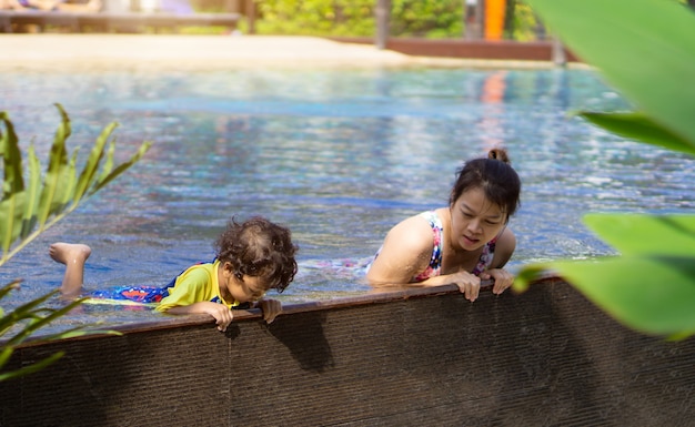 El muchacho asiático del niño aprende nadar en una piscina con la mamá. - Efecto filtro al atardecer.