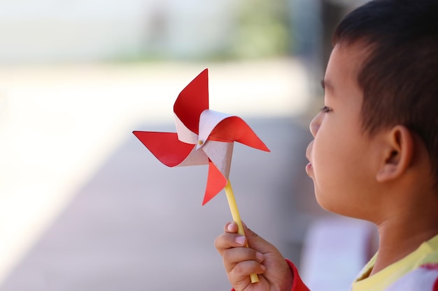 Muchacho asiático que juega con el molino de viento rojo