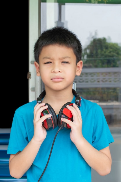 Foto dé el muchacho asiático que sostiene los auriculares en el cuello fondo borroso.