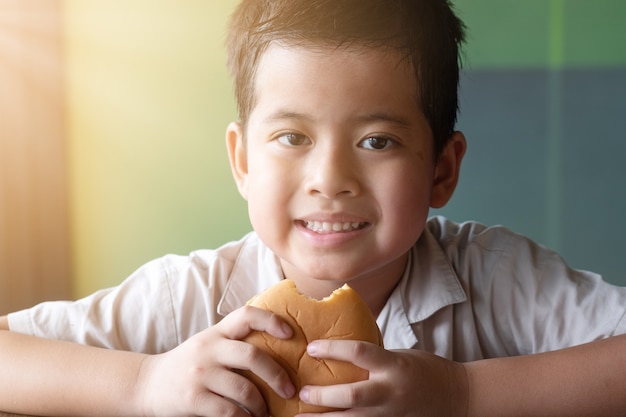 Muchacho asiático del retrato que está comiendo una hamburguesa. Concepto de salud