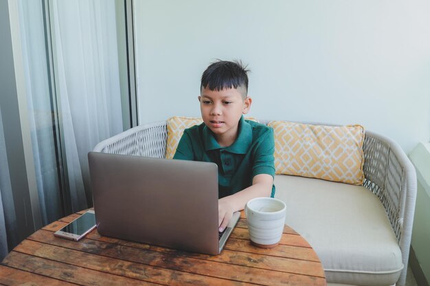 Muchacho asiático serio que hace el trabajo escolar usando la computadora portátil