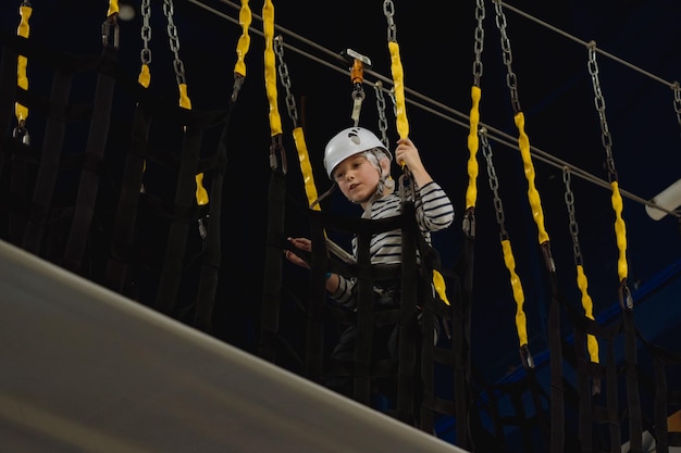 Muchacho caucásico escalada en parque de aventuras pasando carrera de obstáculos parque de cuerdas altas en el interior