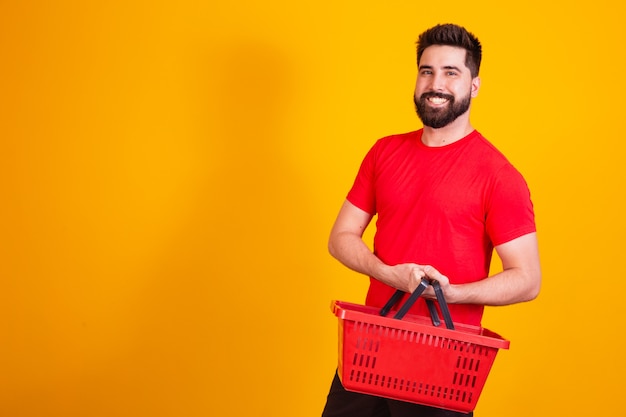 Muchacho caucásico hermoso que sostiene una cesta de la compra en fondo amarillo. concepto de compras