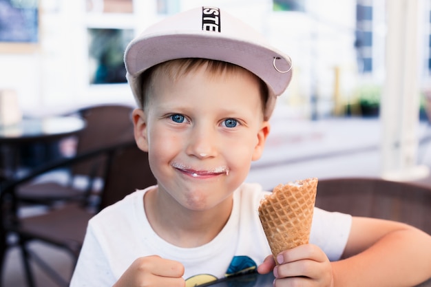 Foto el muchacho está comiendo el helado en una taza de la galleta que se sienta en una tabla en un café al aire libre. día de verano.