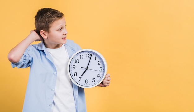 Muchacho contemplado que sostiene el reloj blanco en la mano que mira lejos