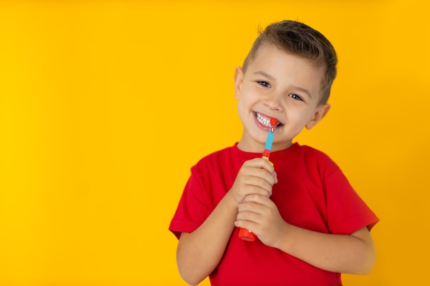 El muchacho se está cepillando los dientes con cepillo de dientes sobre fondo amarillo.