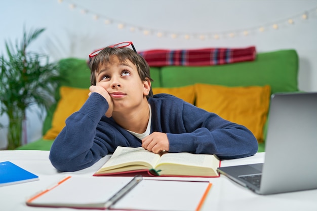 Un muchacho estudiante cansado que estudia en casa, pensativo mirando hacia arriba