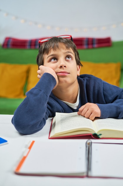 Un muchacho estudiante cansado que estudia en casa, pensativo mirando hacia arriba