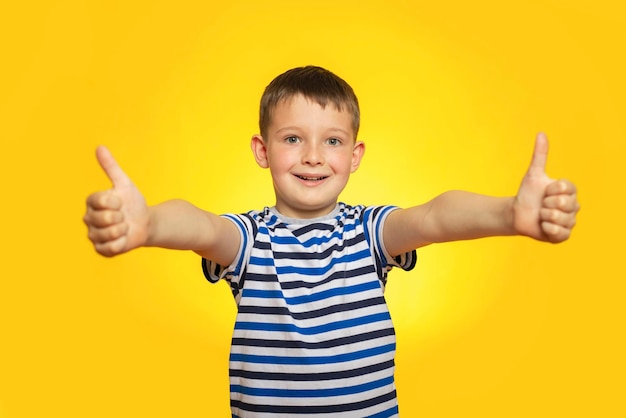 Muchacho feliz en camiseta a rayas mostrando pulgares arriba gesto sobre fondo amarillo