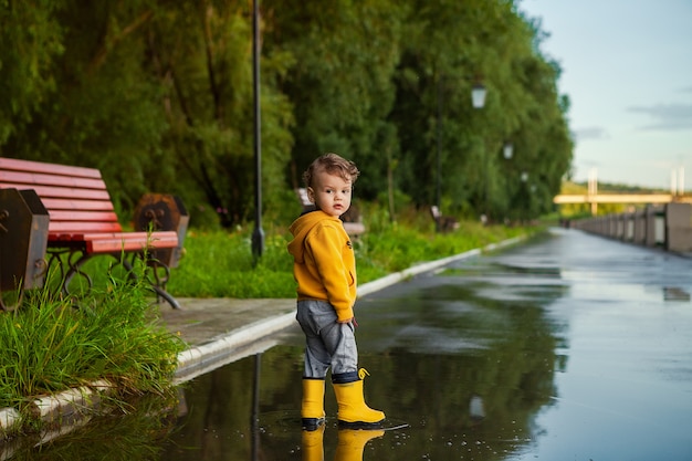 Muchacho feliz del niño con las botas de goma en charco en un paseo de la primavera.