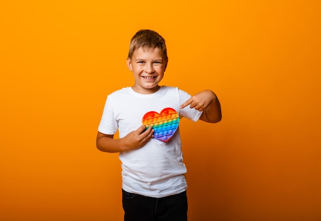 Muchacho feliz que sostiene el juego pop it en las manos, aislado sobre fondo amarillo. Niño alegre con pop