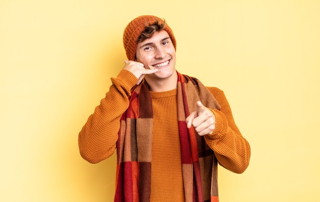 Muchacho joven adolescente sonriendo alegremente y apuntando a la cámara mientras hace una llamada, gesto más tarde, hablando por teléfono