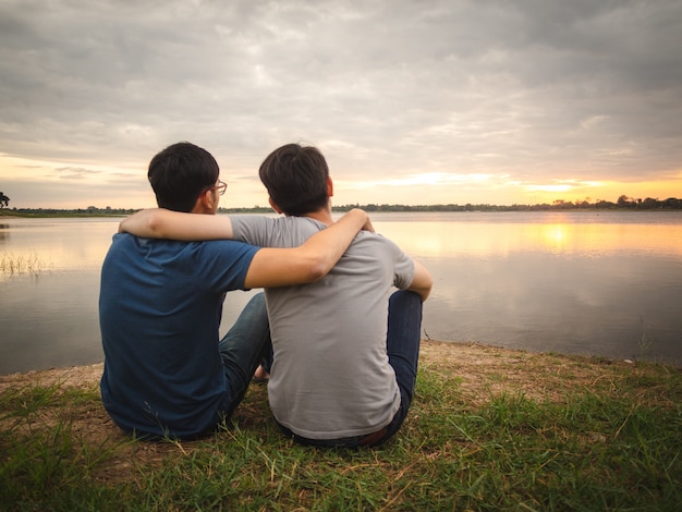 Muchacho joven que se sienta al lado del lago y que mira la puesta del sol. Concepto de amistad